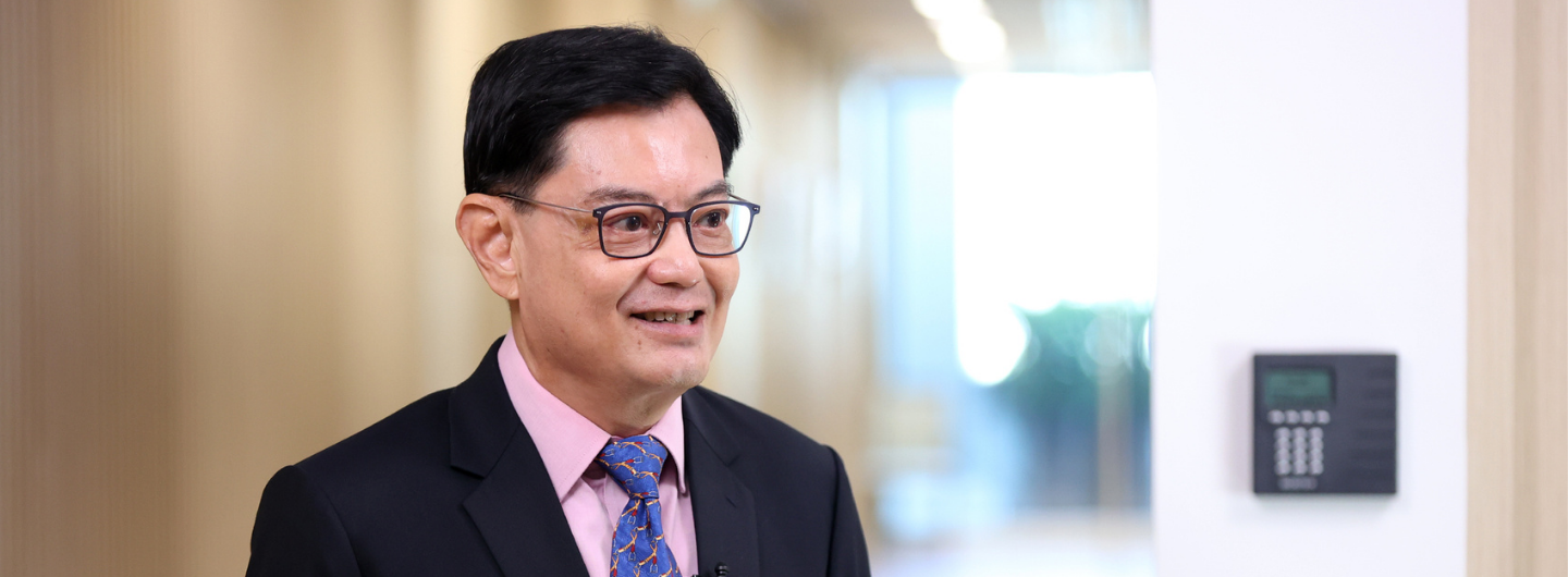 Man in suit and glasses, wearing a blue tie with red accents, indoors.